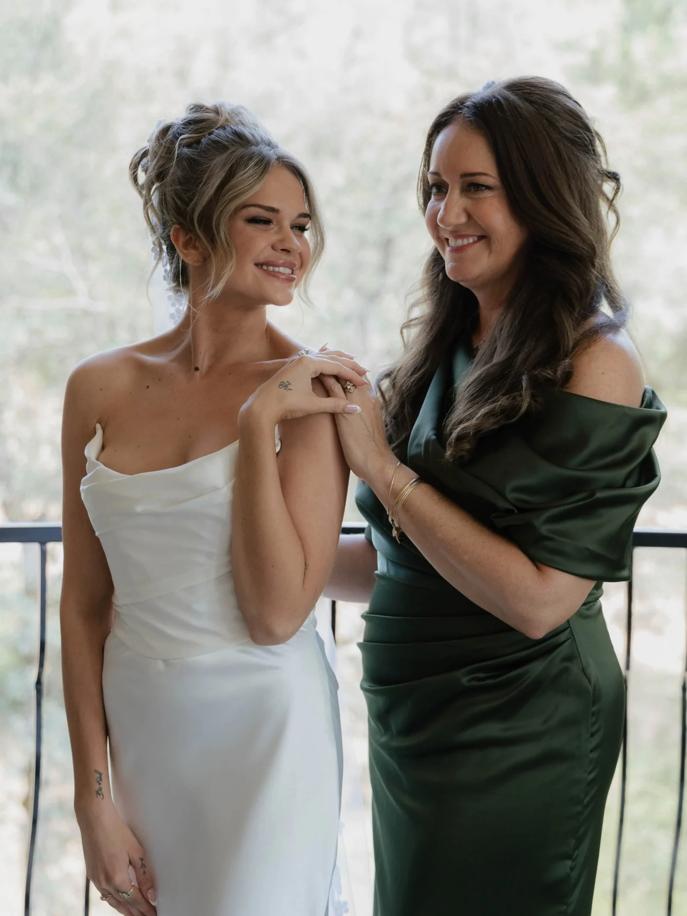 Bride with a natural warm glow beside a woman in an emerald dress